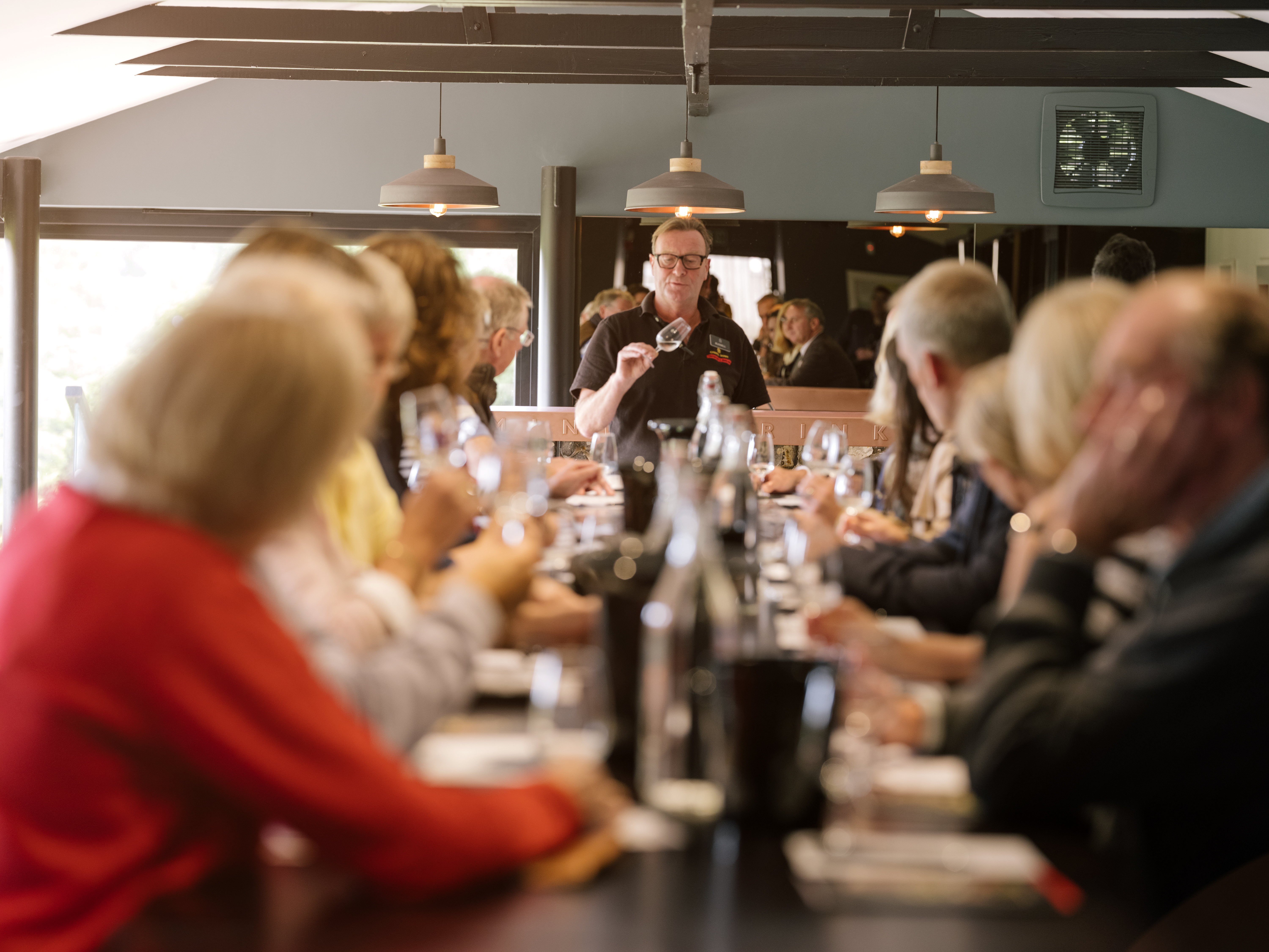 Large group of people sitting at long table at wine tasting.