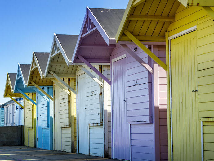 Row of colourful beach huts with blue sky above.
