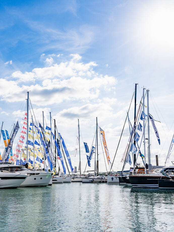 Several sailboats with colorful flags docked at a marina under a bright sky with sun and scattered clouds.