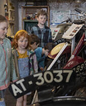 Children looking at vintage motorcycles and signs in a museum exhibition with classic vehicles and motoring memorabilia on display.