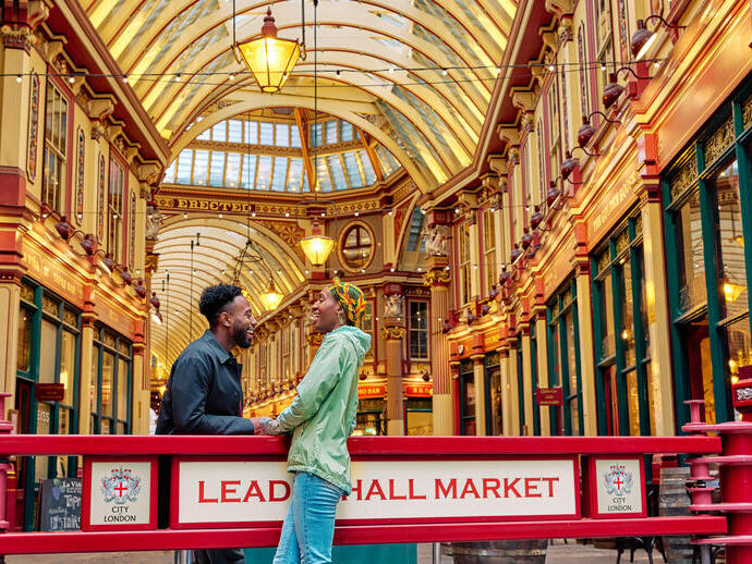 Smiling couple engaged in conversation outside a market hall with an ornate decorated gold ceiling.