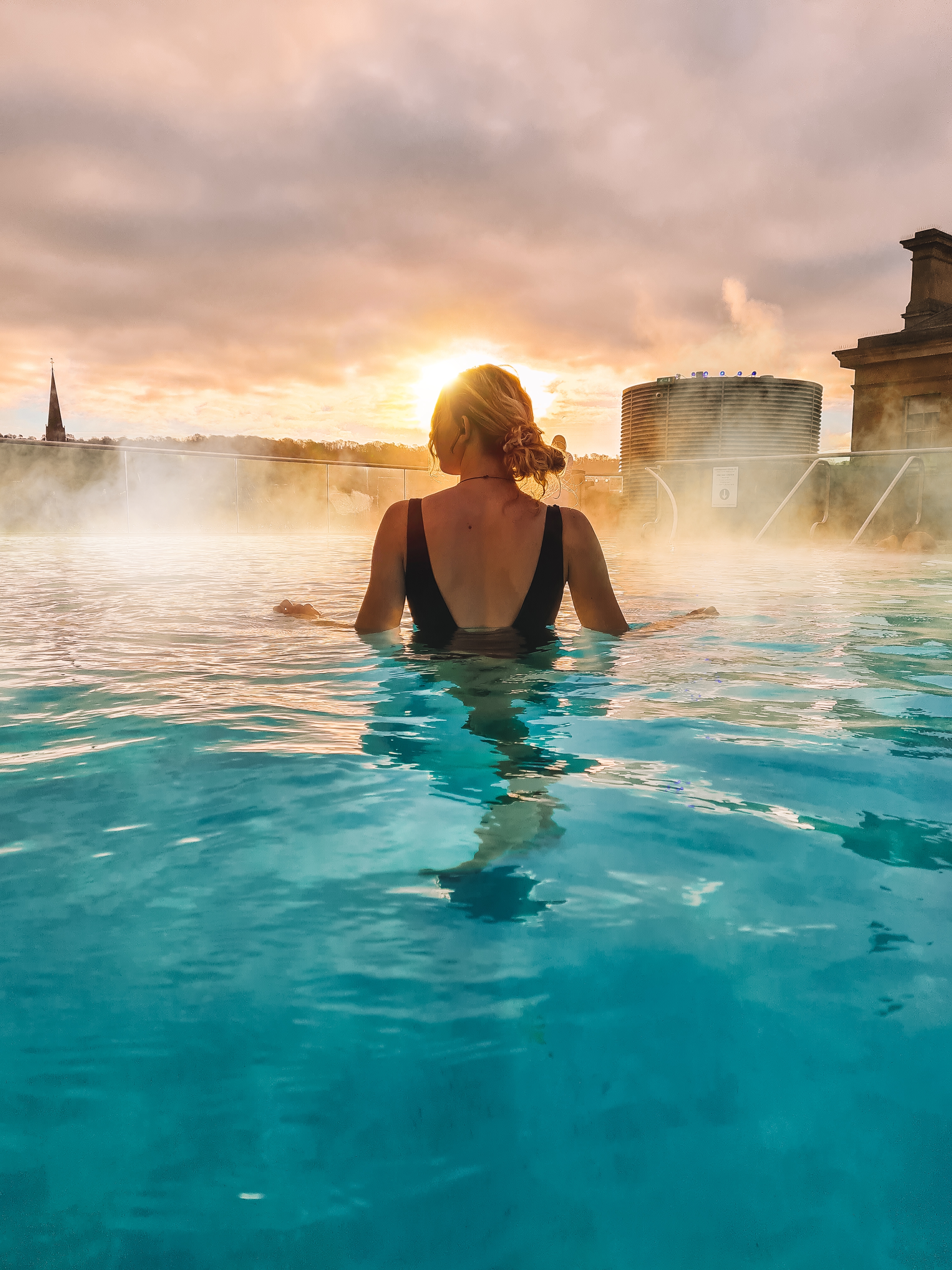 A woman stands looking out to a view in the rooftop pool at sunrise