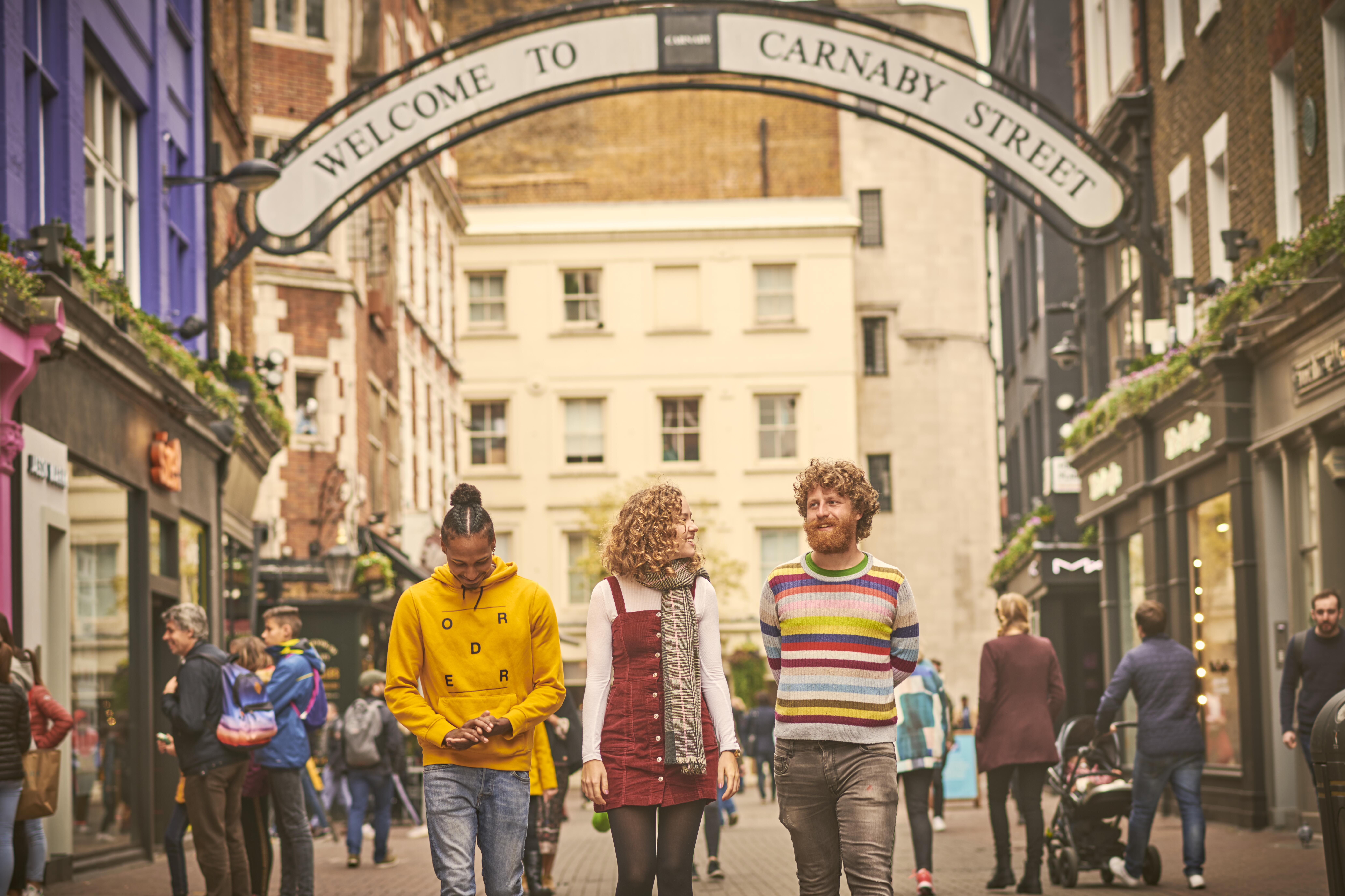 Une femme et deux hommes marchant dans une rue commerçante