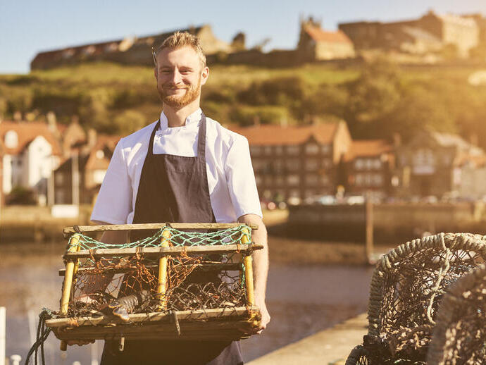 Man holding a lobster trap on a pier in the sunshine