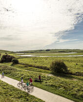 A family cycling along path through the wide open grassy English landscape.