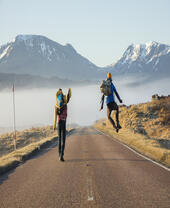 Two men walking and jumping on a road surrounded by mountains