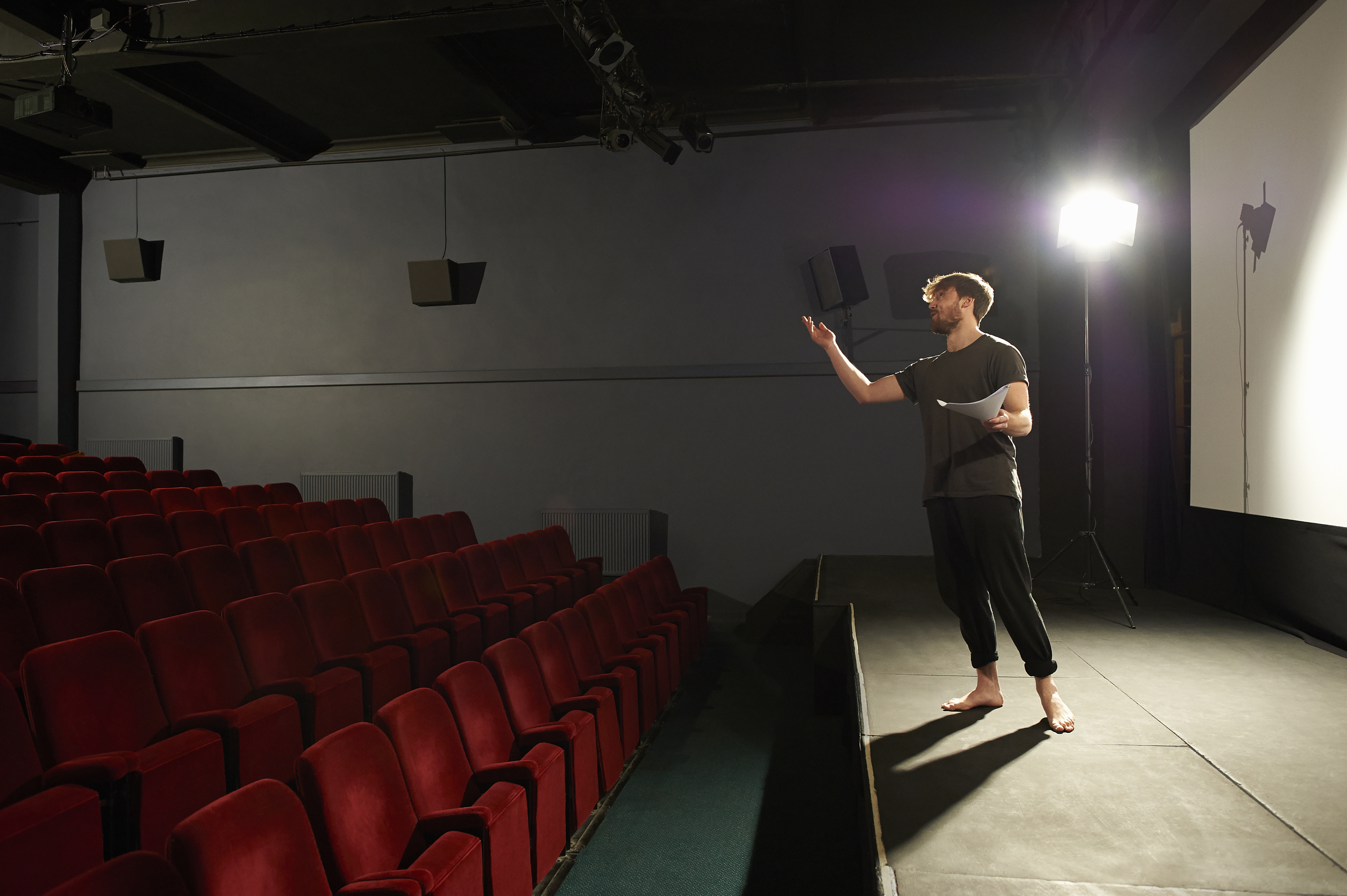 An actor rehearses his lines on a spotlit stage in a small community theatre.
