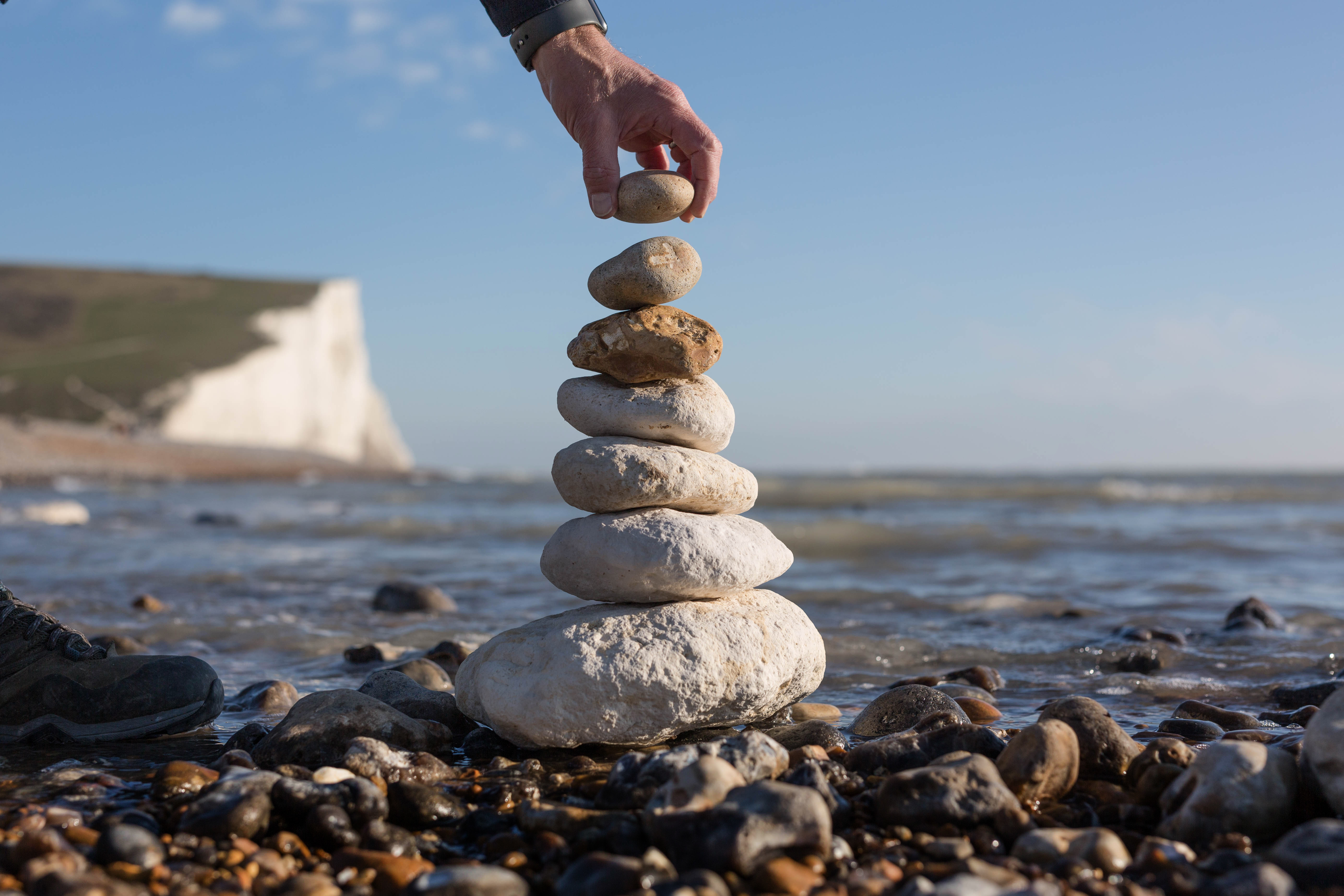 A hand posing with a stack of stones on the coast with white cliffs in the background
