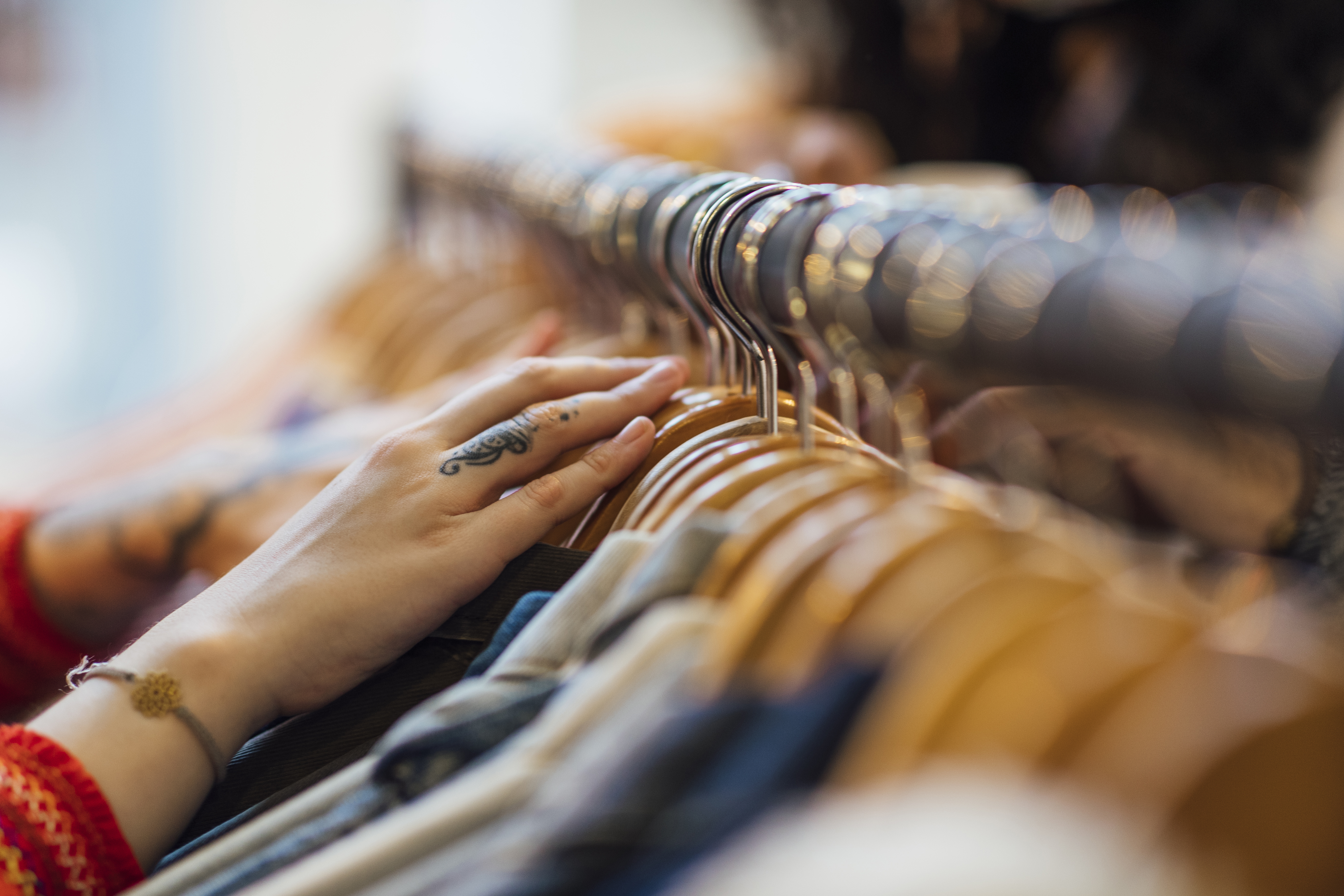 A close up shot of hands sifting through clothing hanging on a clothes rack in a clothes shop.