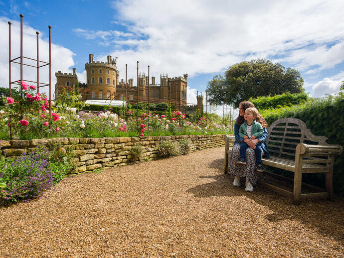 A woman sits on a bench with her child on her lap in front of a castle 