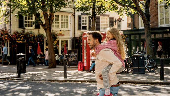 Ein Mann läuft mit einem Kind auf dem Rücken, im Hintergrund ist ein Platz zu sehen.