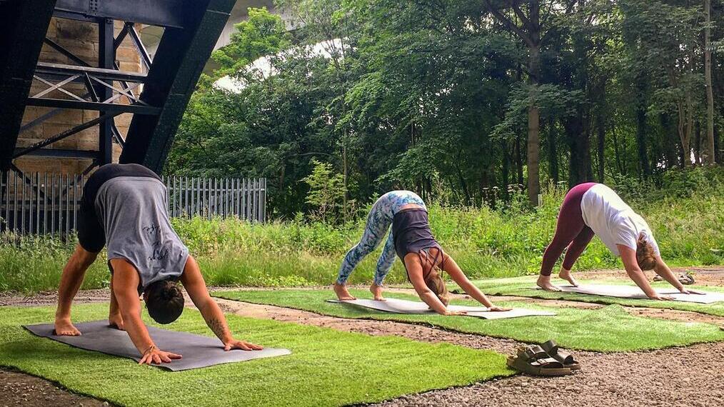 People practising yoga outside, beneath a bridge