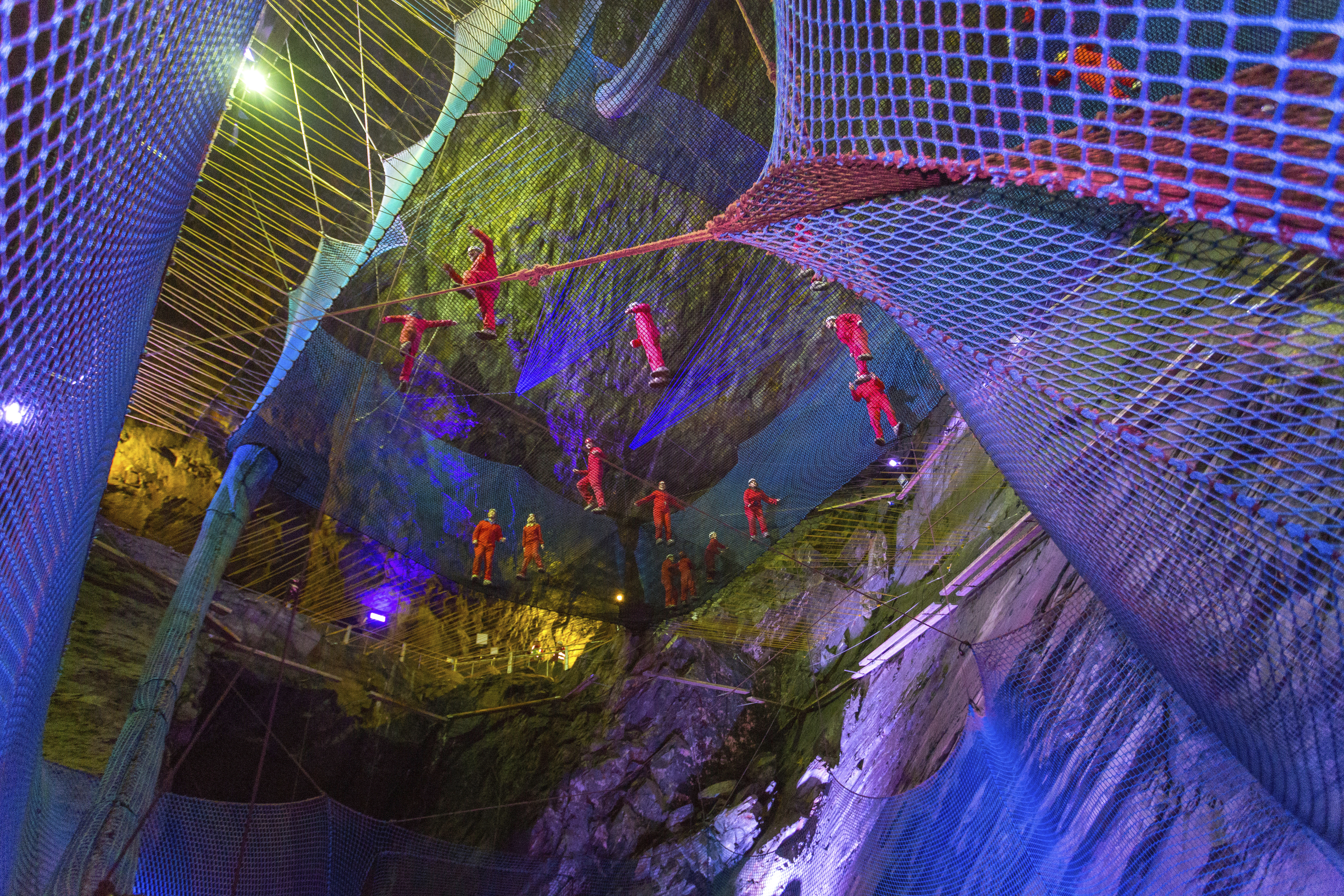 Group of people bouncing on net trampolines suspended in deep caverns