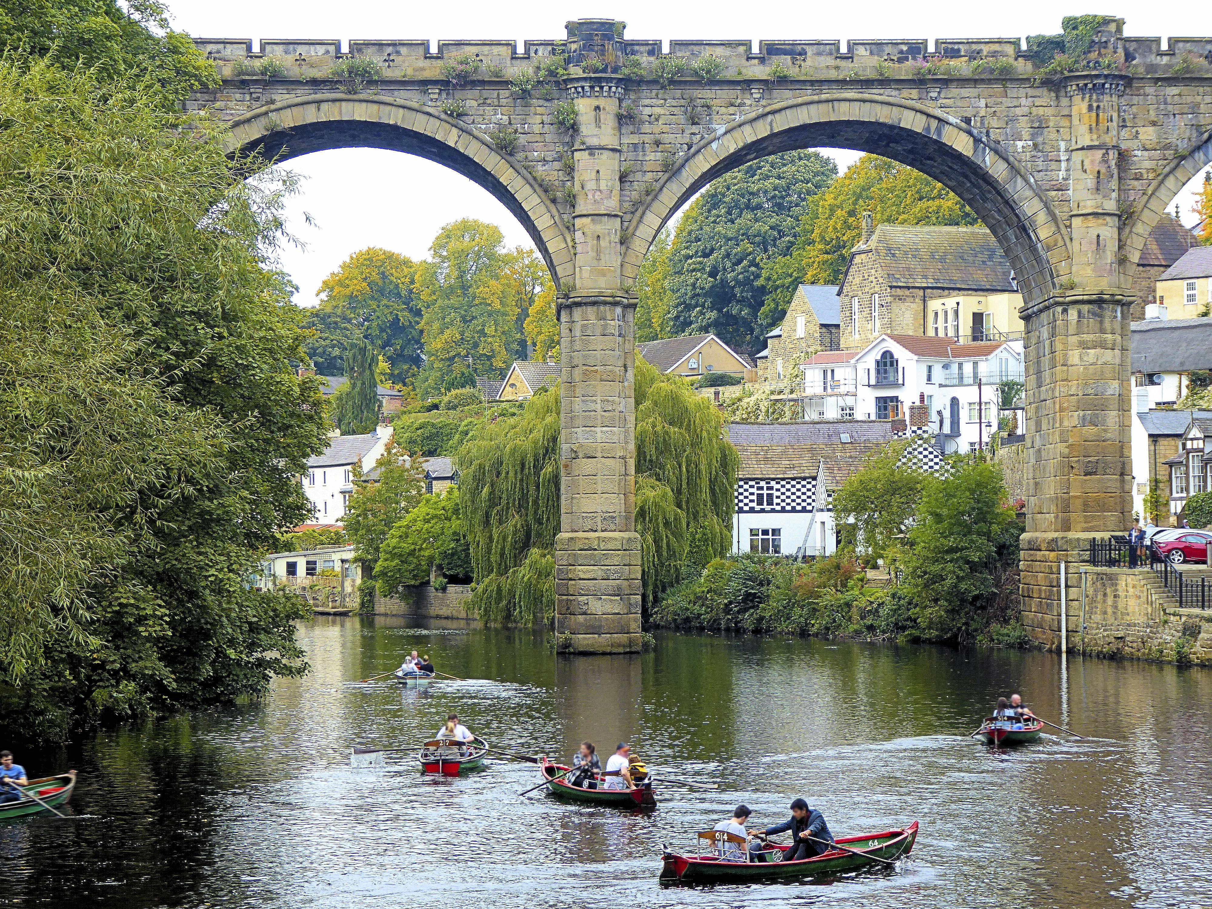 Menschen in Ruderbooten auf einem Fluss neben einem Viadukt in einer Stadt