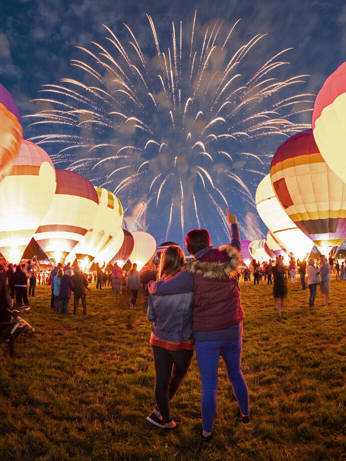 Coppia che osserva mongolfiere a terra e fuochi d'artificio nel cielo notturno