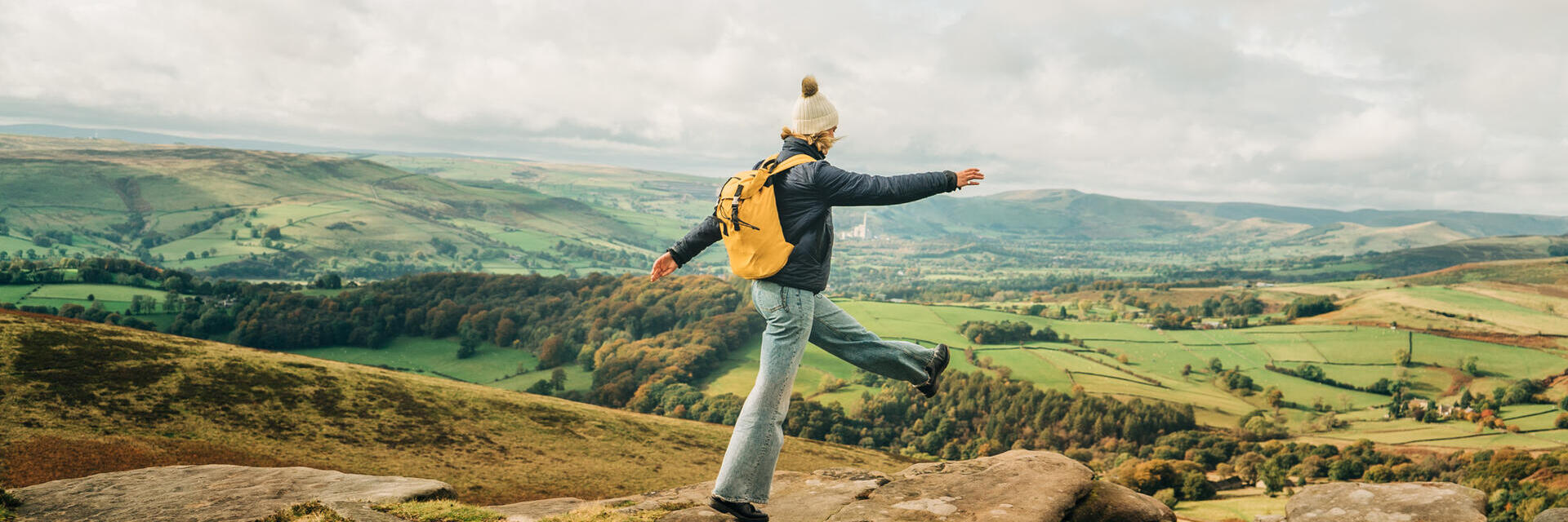 Woman skipping on rocks at edge of hill. Landscape view
