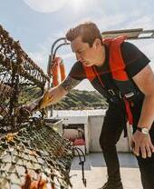 Man on boat looking into a crab net, Haar, Scotland.