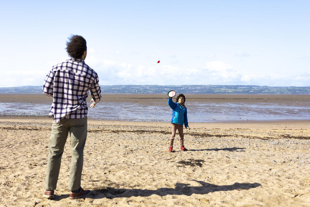 A man and a boy play a ball game on a beach