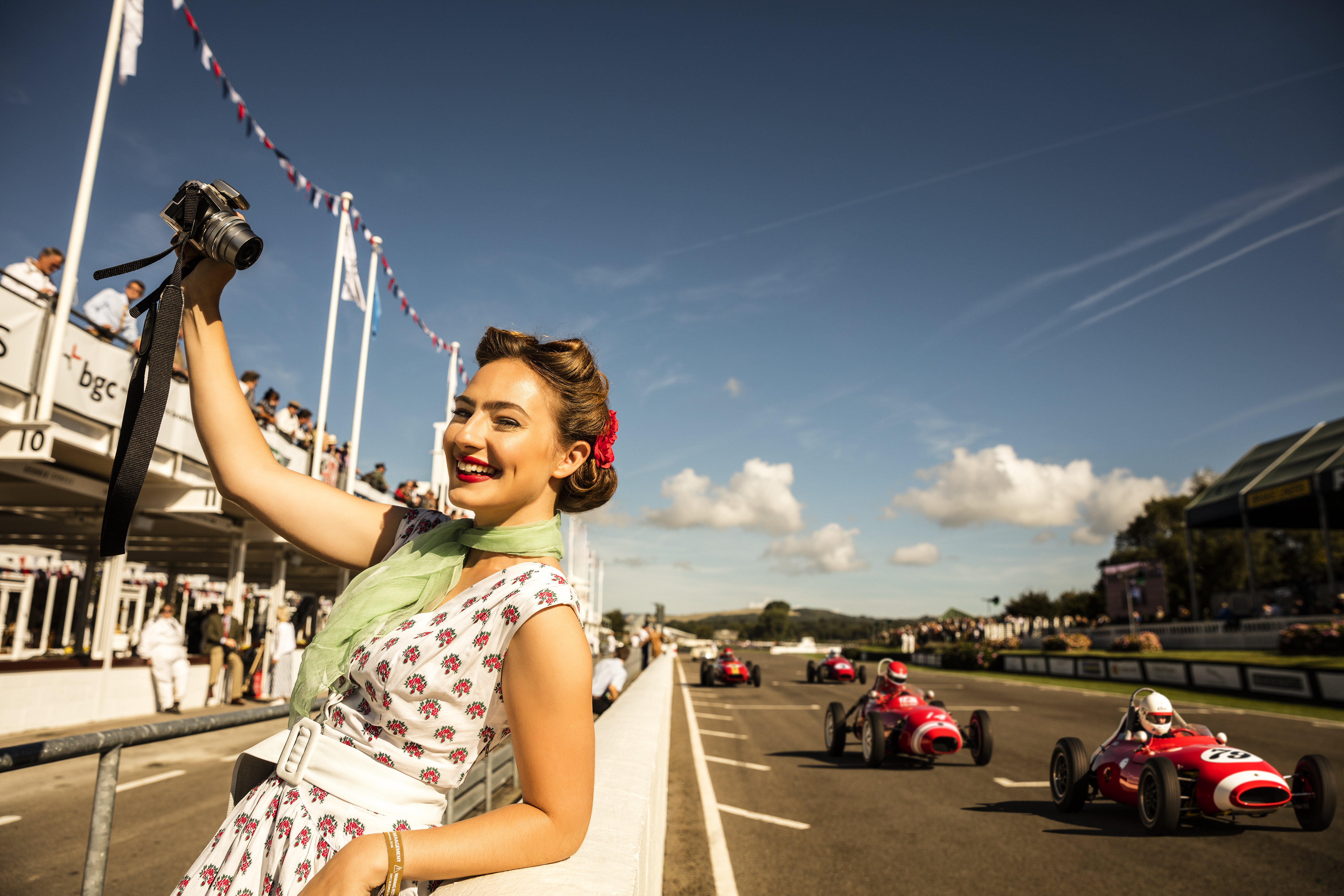 Woman taking a selfie in vintage dress standing by a car racing track