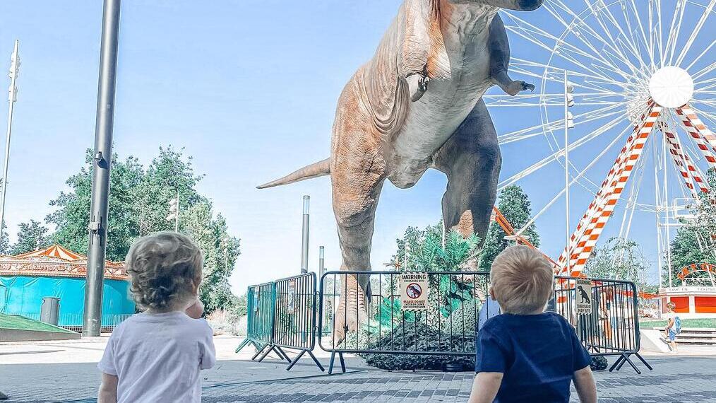 Deux enfants regardant un modèle de dinosaure dans une fête foraine