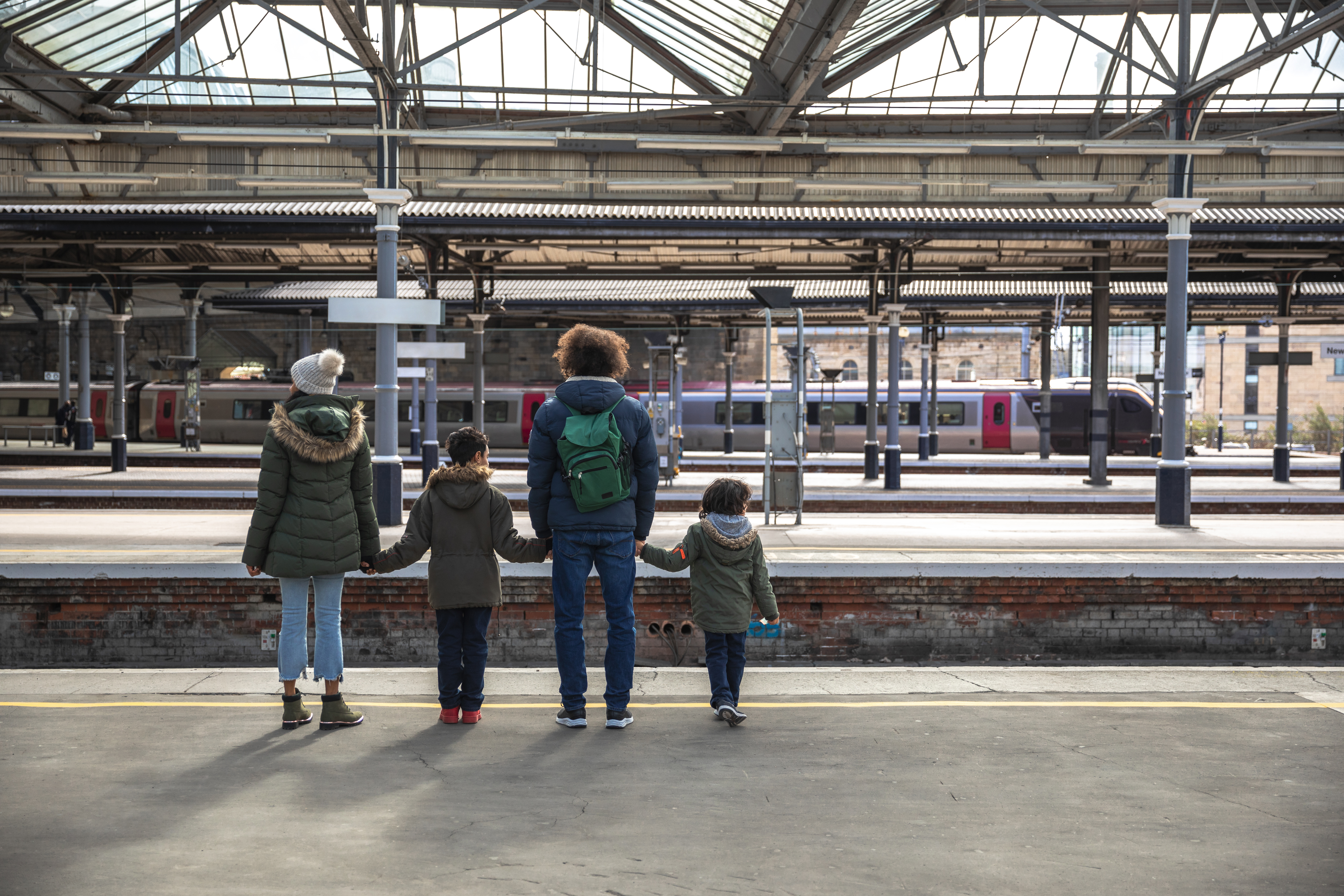 Eine multikulturelle vierköpfige Familie, bestehend aus Mutter, Vater und ihren beiden kleinen Söhnen, steht auf dem Bahnsteig des Bahnhofs von Newcastle und wartet auf ihren Zug.