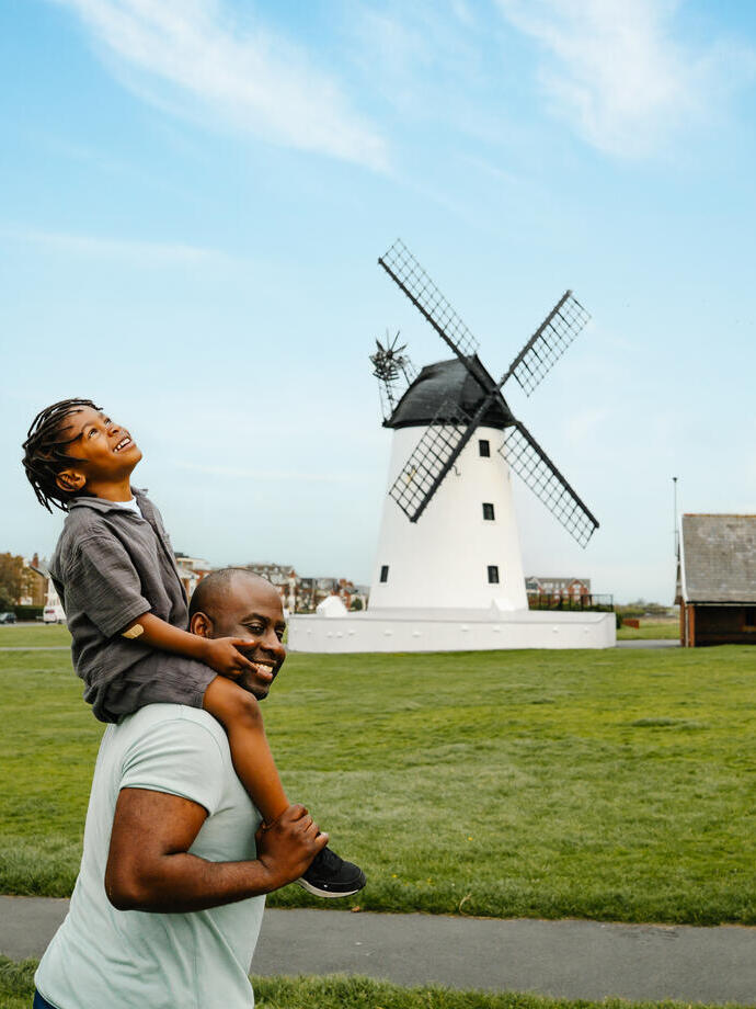A father and son have fun in a field in front of a windmill