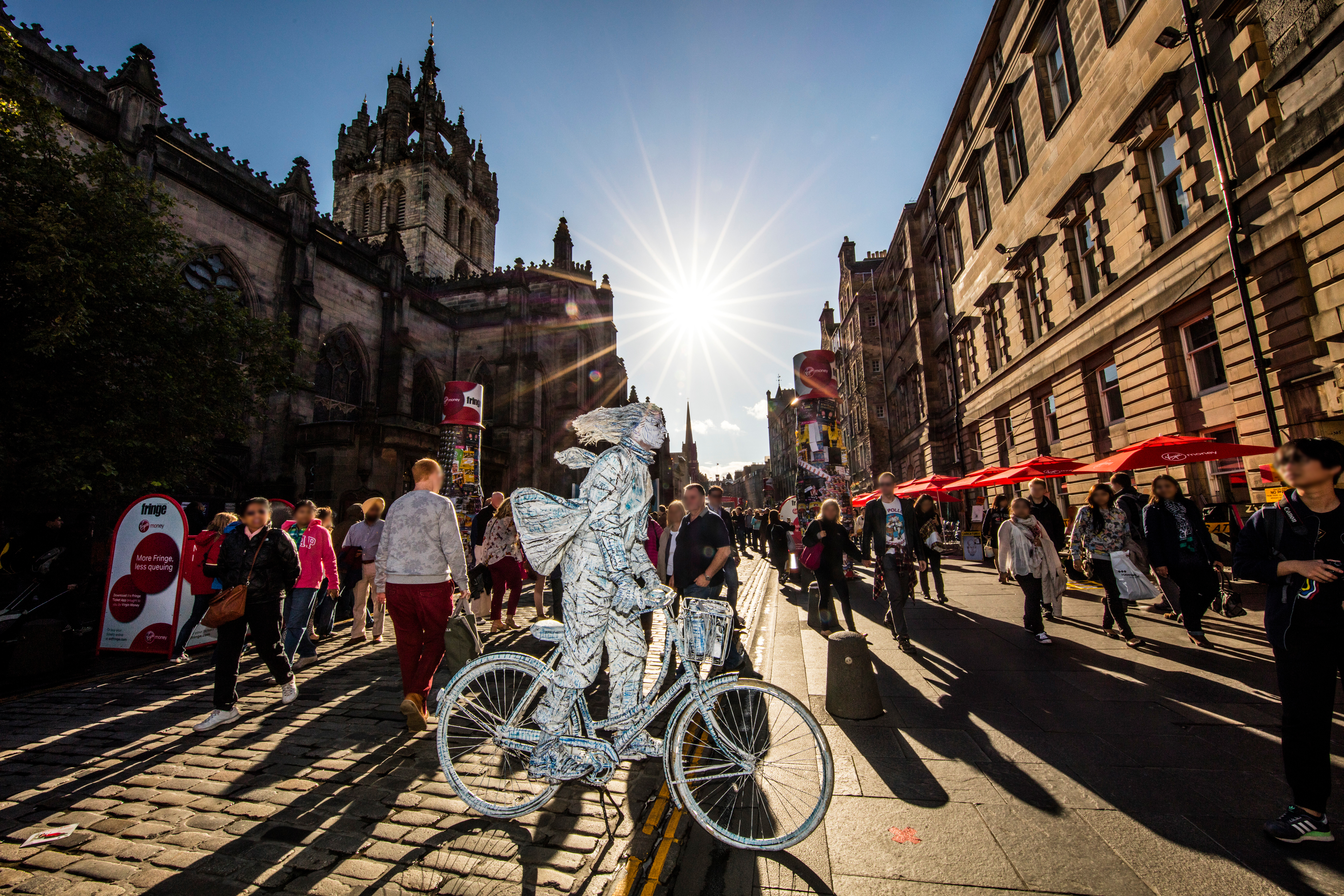 Man in silver on a bicycle in costume drawing a crowd