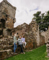 Due donne e un uomo seduti sulle rovine di un grande castello con giardino.