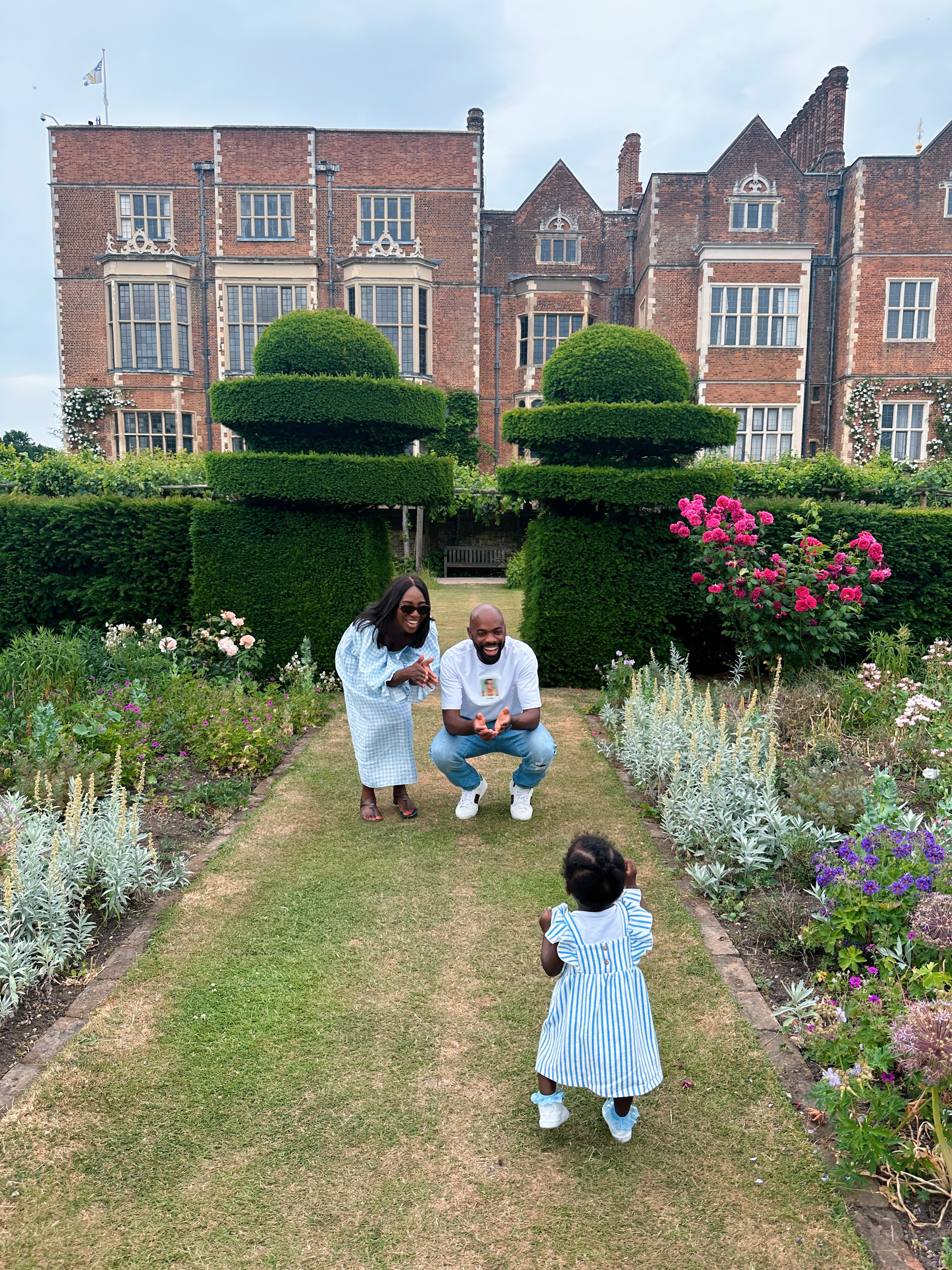 Man, woman and child playing in formal garden of large country house