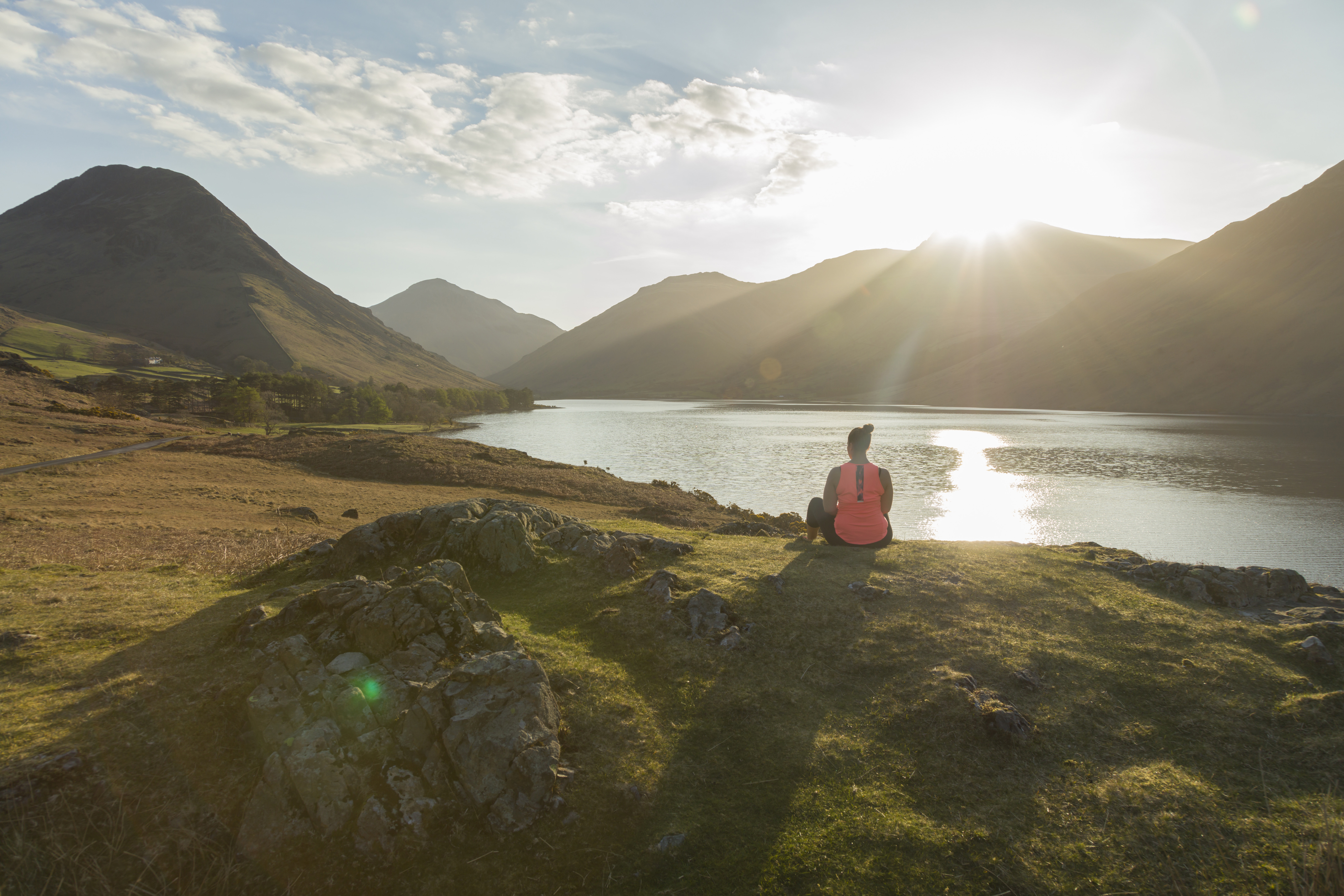 Woman, meditating in green valleys, near lake. The sun is shining.