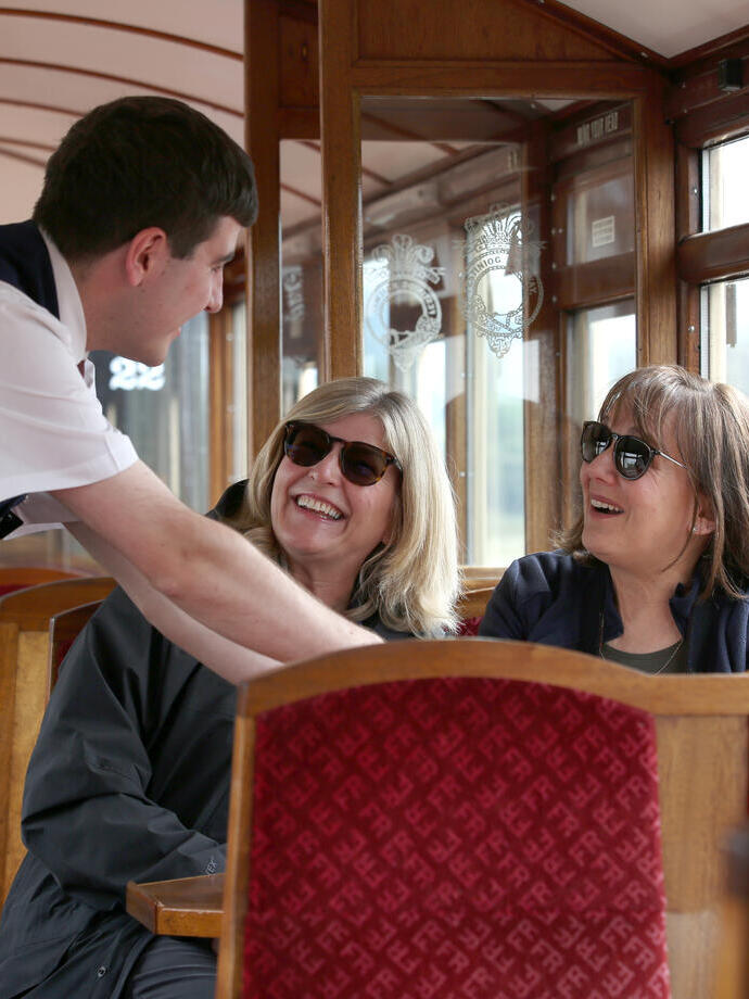 Pasajeros de un tren histórico hablando con un miembro de la tripulación.