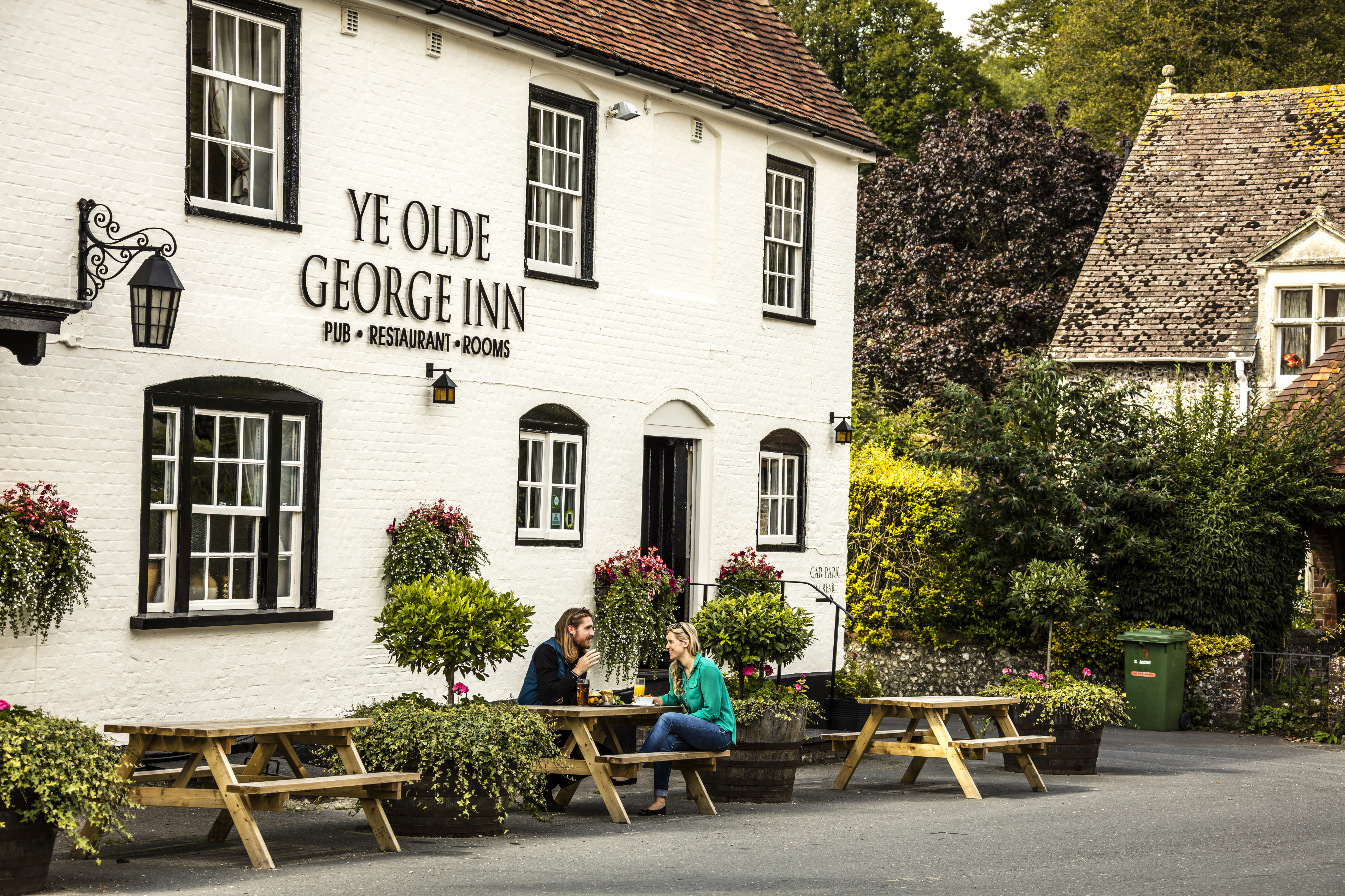 A couple sitting outside a pub on a bench having a drink and eating a meal
