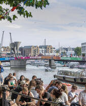Crowds of people sitting on the harbourside in Bristol, watching ships go past
