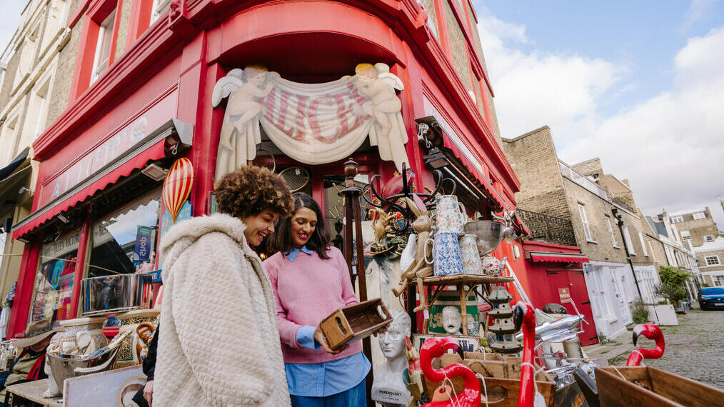 Two women browsing outside an antique and bric-a-brac store piled high with fun goodies.