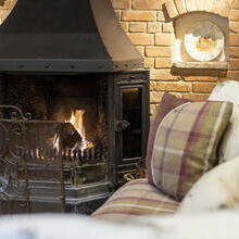 Close-up of the inglenook fireplace with fire and tartan patterned sofas.