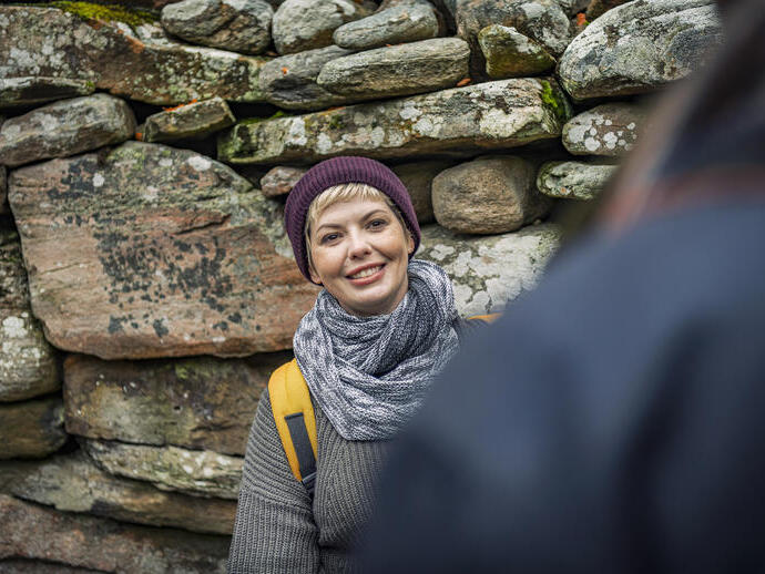 Femme portant un chapeau et une écharpe posant devant un mur de pierre
