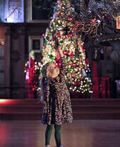 A girl looking at a hanging ornament in front of a decorated christmas tree at Bamburgh Castle's Christmas Kingdom