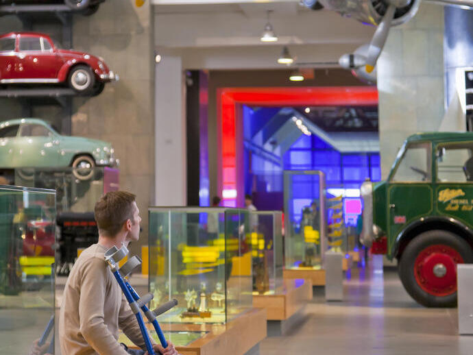 Man sitting down, looking at the displays in a museum holding his crutches