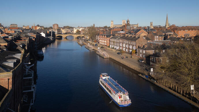 Un bateau descend une rivière vers un pont avec la ville en arrière-plan