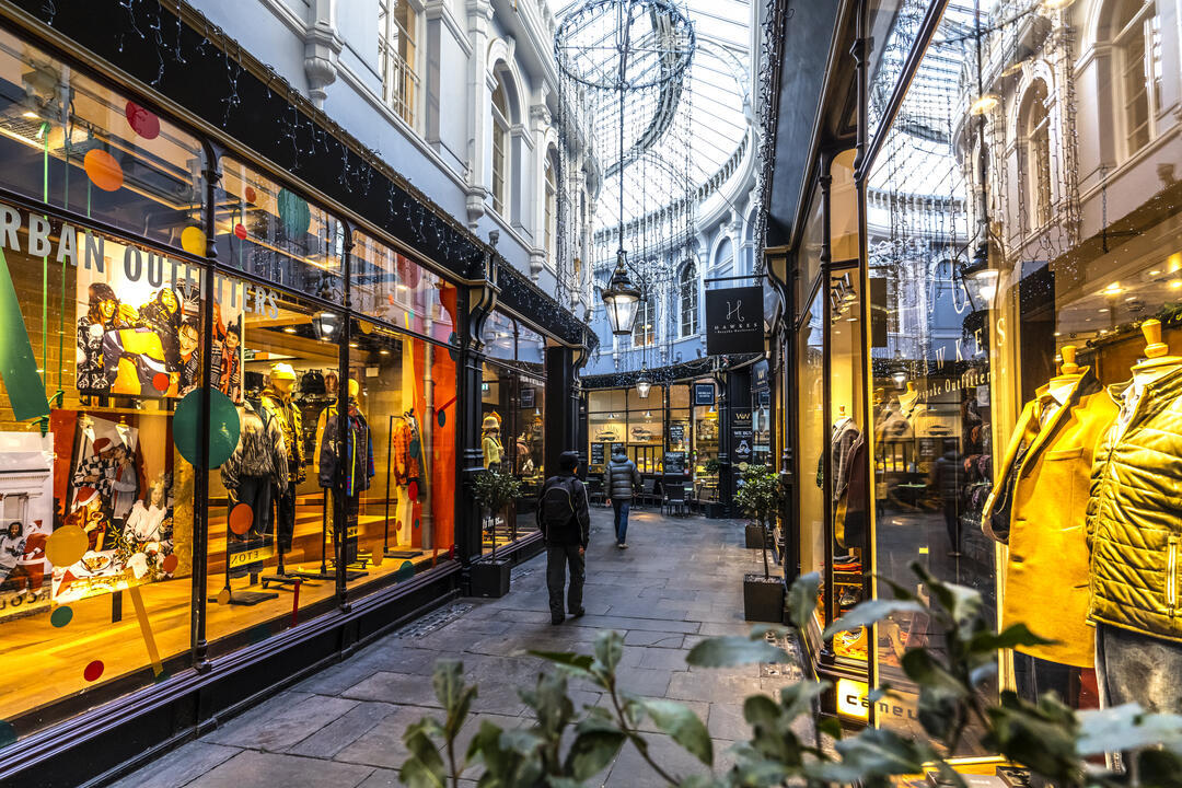 Menschen, die zwischen Geschäften in einer von innen beleuchteten Passage spazieren gehen