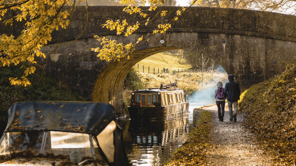 Hombre y mujer caminando junto a un canal cerca de un puente bajo