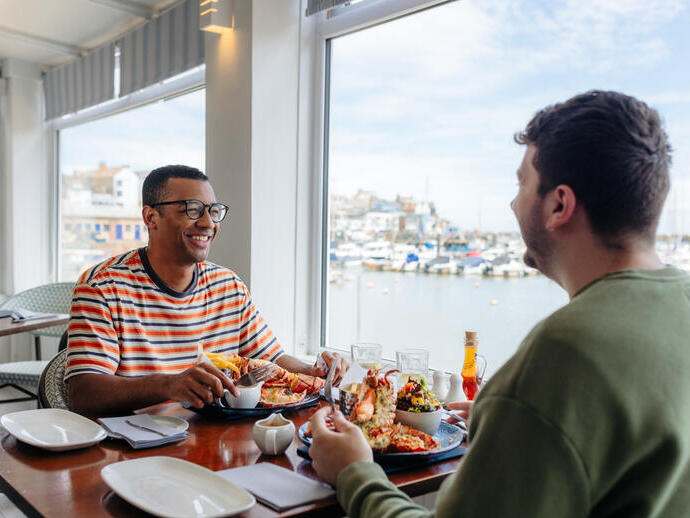 Two men eat lobster in a restaurant with a harbour view