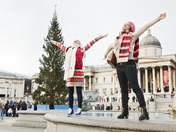 Women standing on the rim of a fountain in a city square at Christmas