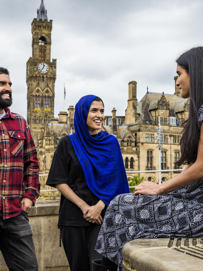 Zwei Frauen und ein Mann stehen vor einer Stadtansicht und unterhalten sich.