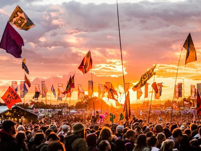 Festival de Glastonbury, montrant une foule de personnes au coucher du soleil, agitant des drapeaux