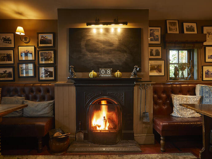 A fireplace in a pub with a lit fire flanked by two leather sofas with tables