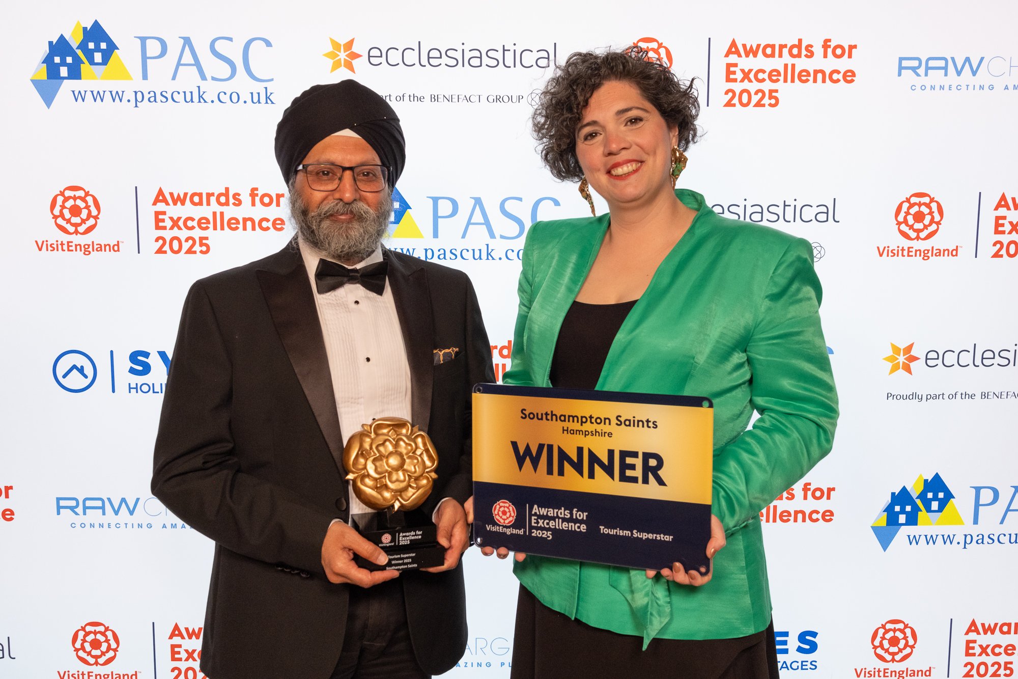 Two winners smiling and posing with their plaque on stage at a gala ceremony.