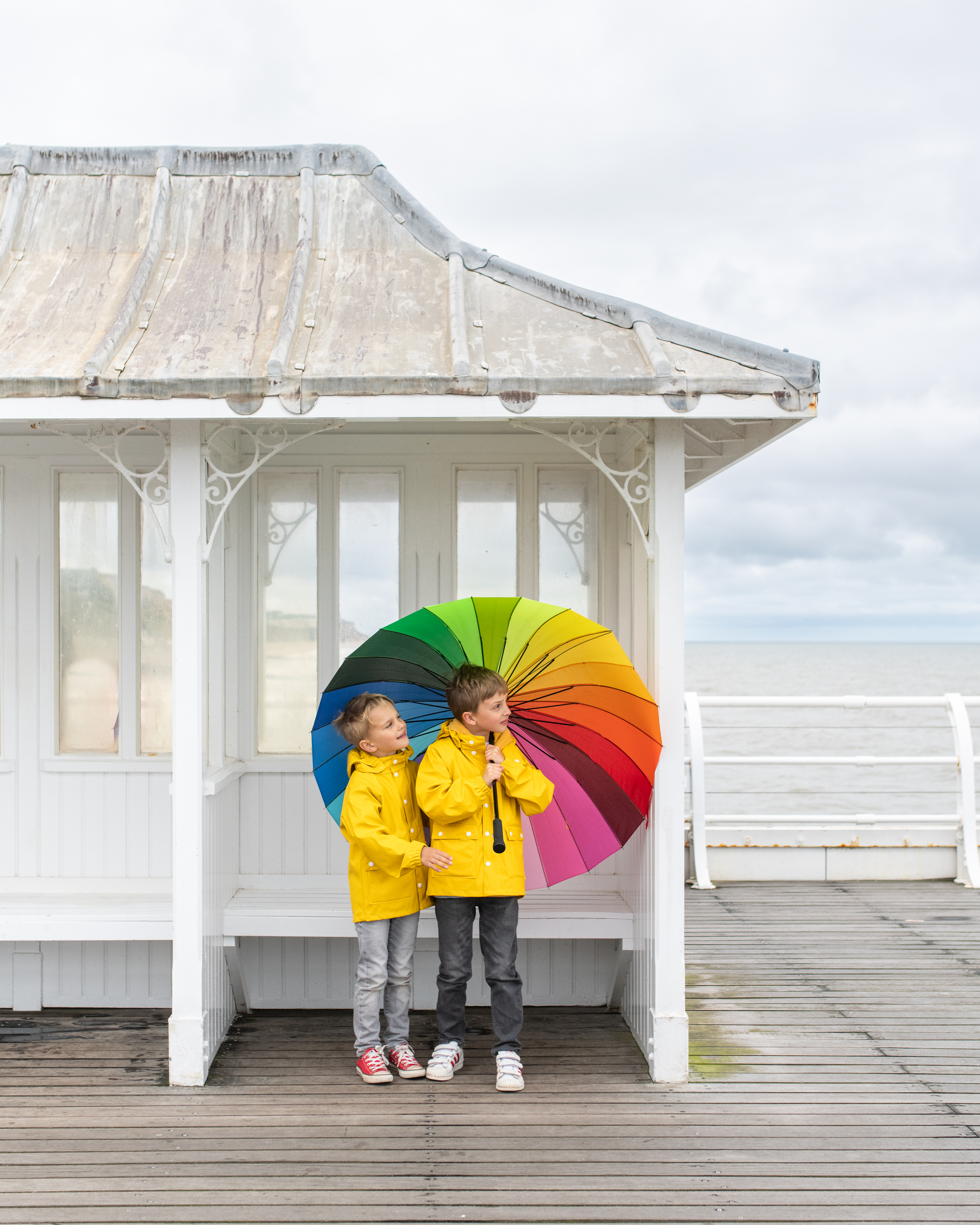 Two children holding an umbrella standing in a shelter on a pier