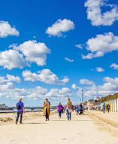 People walking along the coast next to colourful beach huts on a sunny day.