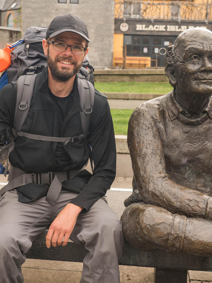 Ein Mann mit Gehstöcken posiert neben einer Statue auf einer Bank in Glasgow